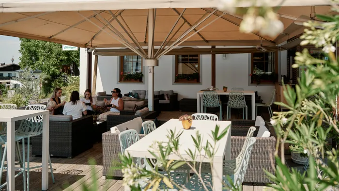 Restaurantterrasse im Freien mit Korbmöbeln und Gästen unter einem großen Sonnenschutz